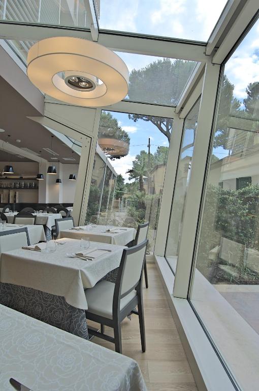a restaurant with white tables and chairs and windows at Zen Hotel Versilia in Marina di Pietrasanta