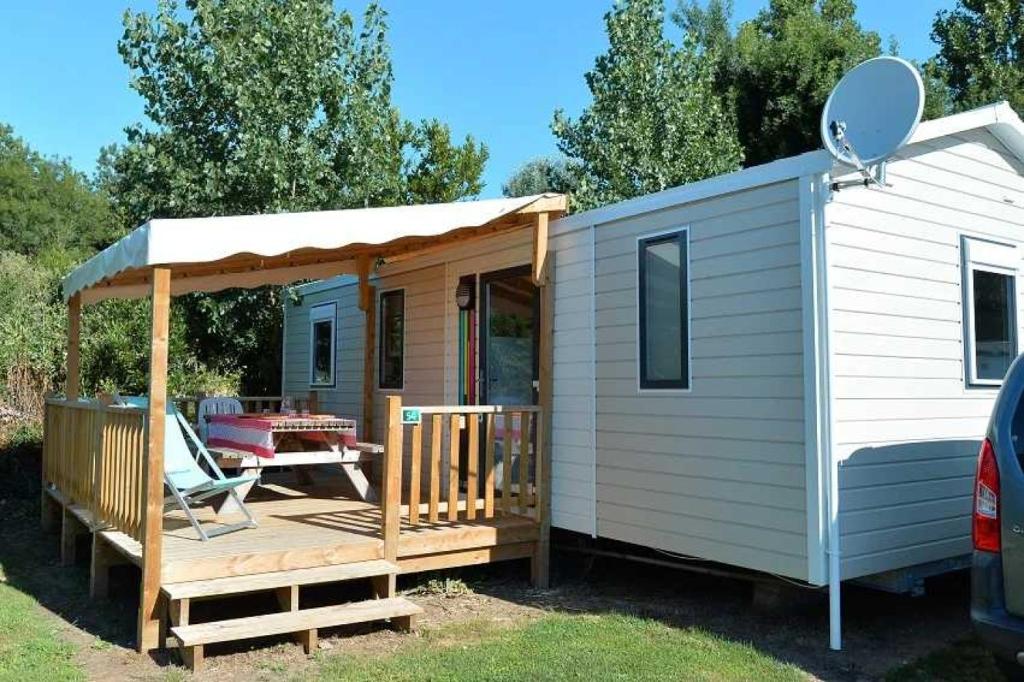 Una pequeña casa con porche y cenador. en Camping 4 étoiles - Parc aquatique - eeibci, en Le Bois-Plage-en-Ré