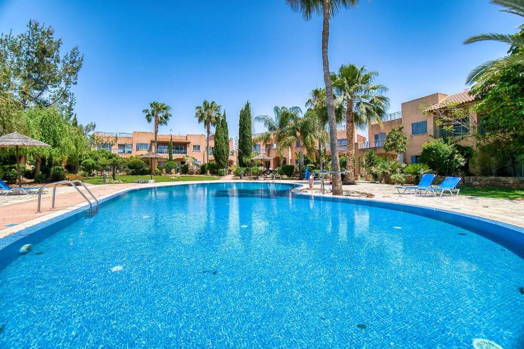 a large blue swimming pool with palm trees and buildings at Mandria Gardens 2 BED in Paphos