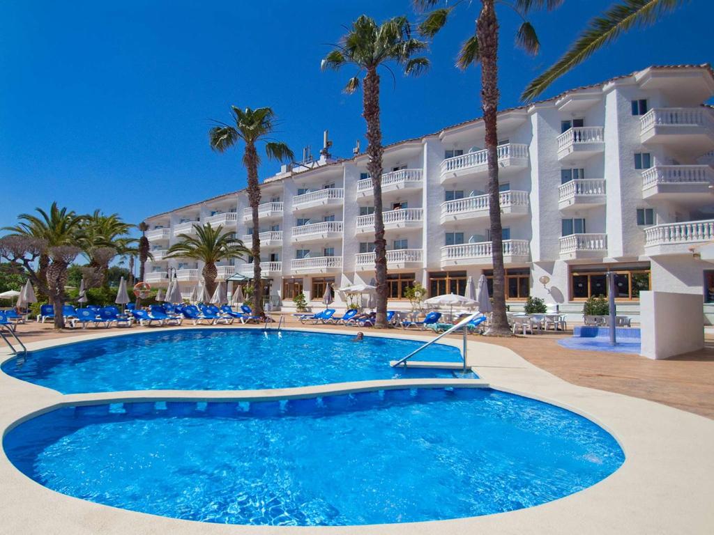a resort with a large swimming pool and palm trees at Hotel Servigroup Romana in Alcossebre