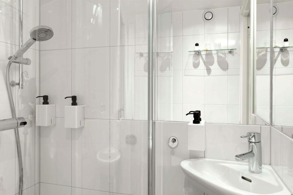 a white bathroom with a shower and a sink at Scandic Malmen in Stockholm