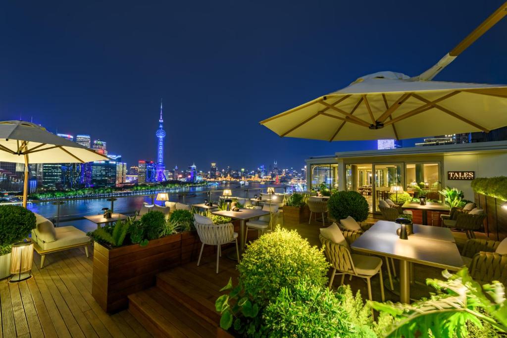 上海上海外滩悦榕庄 - 顶楼露台Tales餐厅酒吧纵览浦江美景的一间晚上带桌子和遮阳伞的餐厅