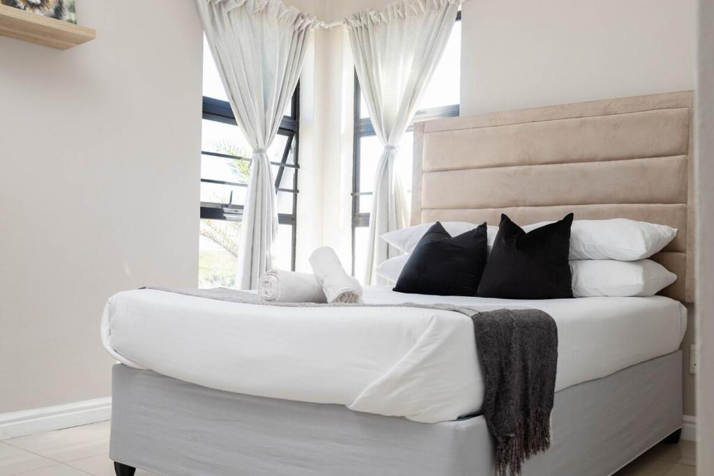 a white bed with black pillows and a window at Bluewater Bay Escape in Gqeberha