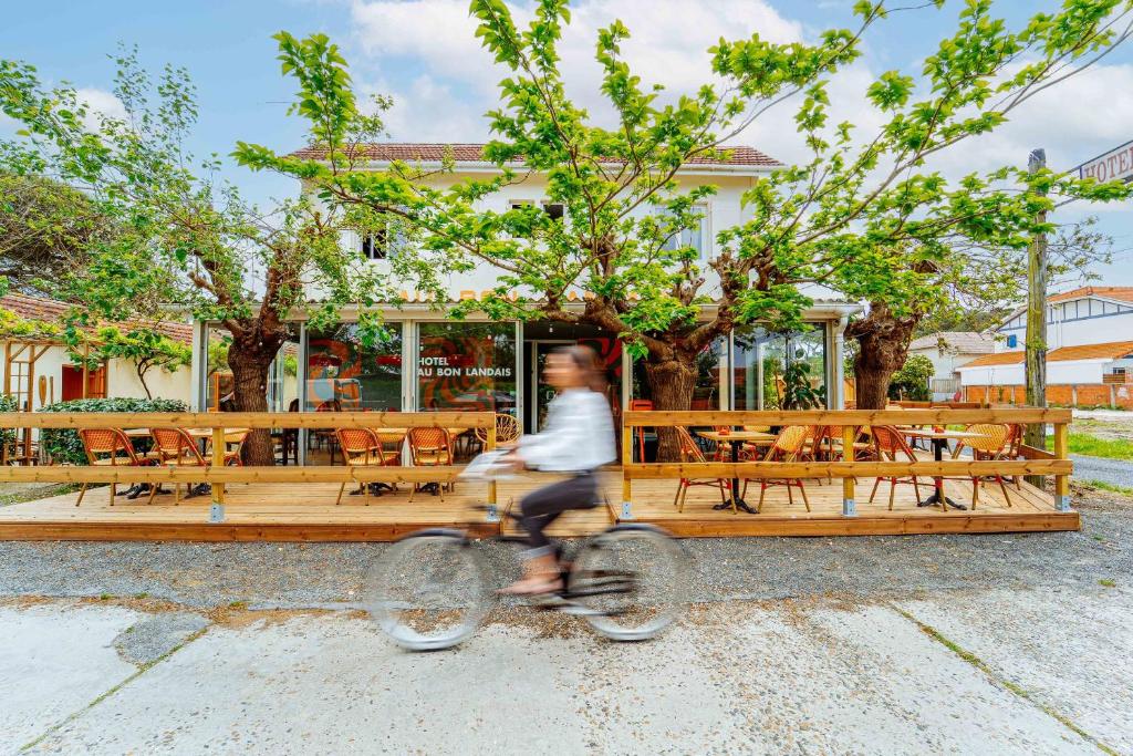 Un uomo che va in bicicletta davanti a un ristorante di Au Bon Landais Surf Hôtel Guinguette a Biscarrosse-Plage