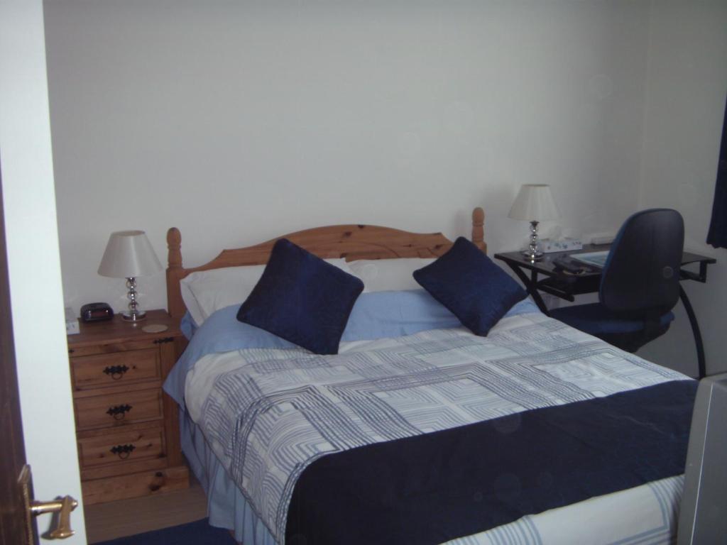 a bedroom with a bed with blue pillows and a desk at Bluebell Cottage in Staines