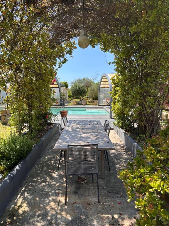 une table et des chaises sous une arche à côté d'une piscine dans l'établissement Belle demeure familiale, à Aigues-Mortes