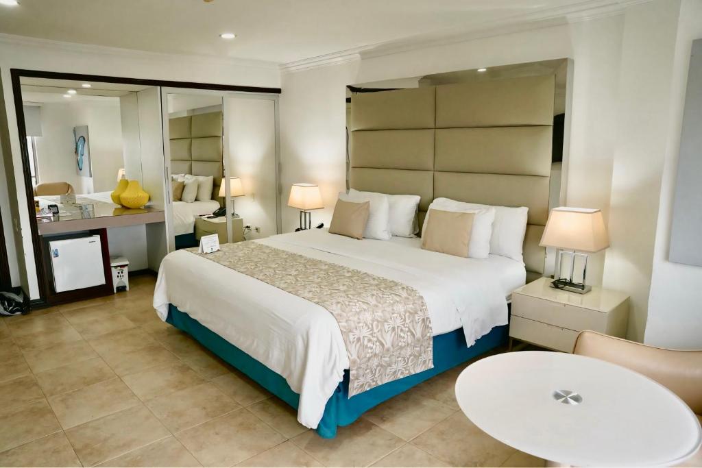 Un dormitorio con una gran cama blanca y un baño. en Hotel Windsor Barranquilla, en Barranquilla