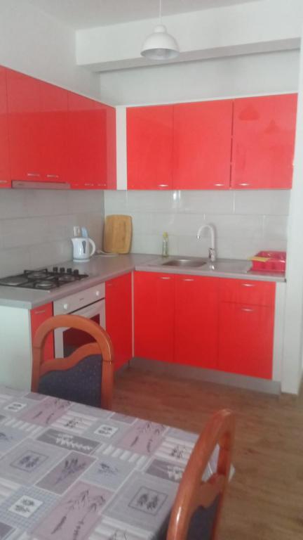 a kitchen with red cabinets and a sink and a table at Apartmani Valentina Drvenik in Drvenik