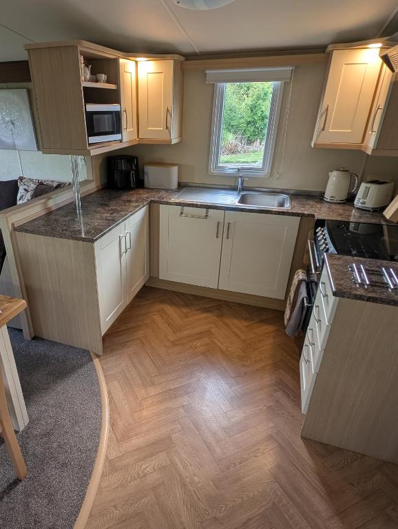 a kitchen with white cabinets and a wooden floor at Red Squirrel Holiday Home in the Countryside, 10 mins to Lligwy Beach in Llandyfrydog
