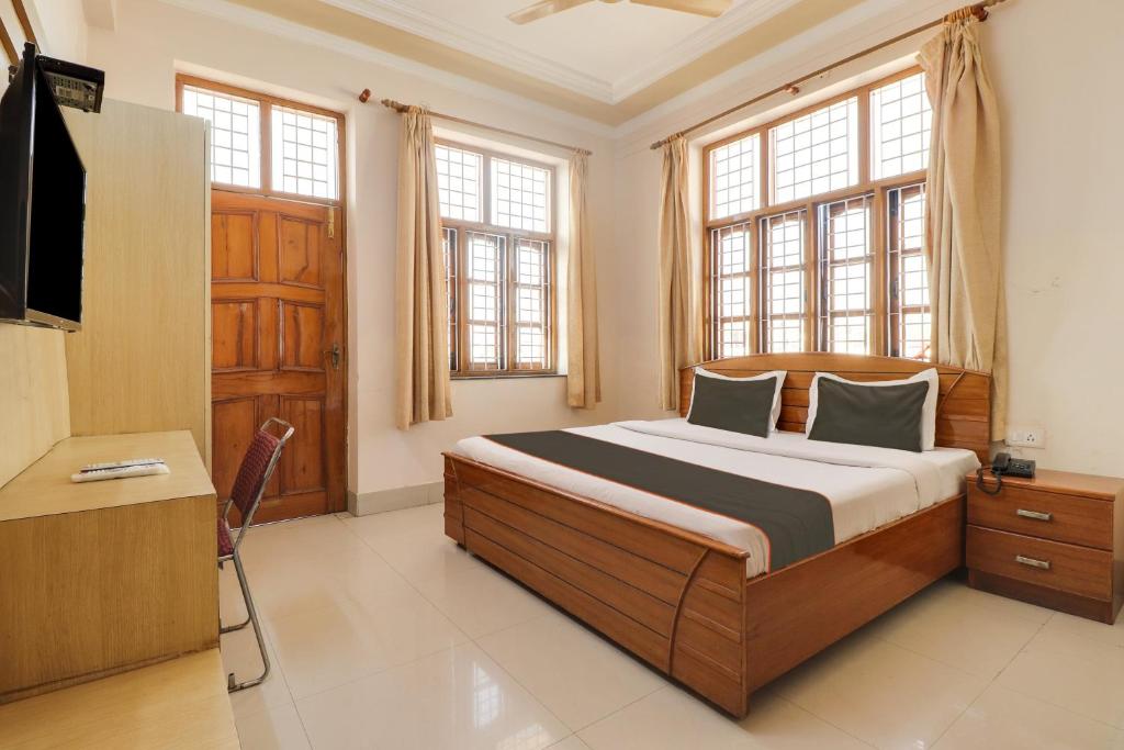 a bedroom with a bed and a tv and windows at Hotel O The Gomti Hotel in Dehradun