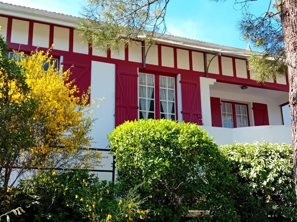 une maison rouge et blanche avec des arbres au premier plan dans l'établissement Maison spacieuse à Capbreton, proche port et plages, jusqu'à 6 personnes - FR-1-239-1122, à Capbreton