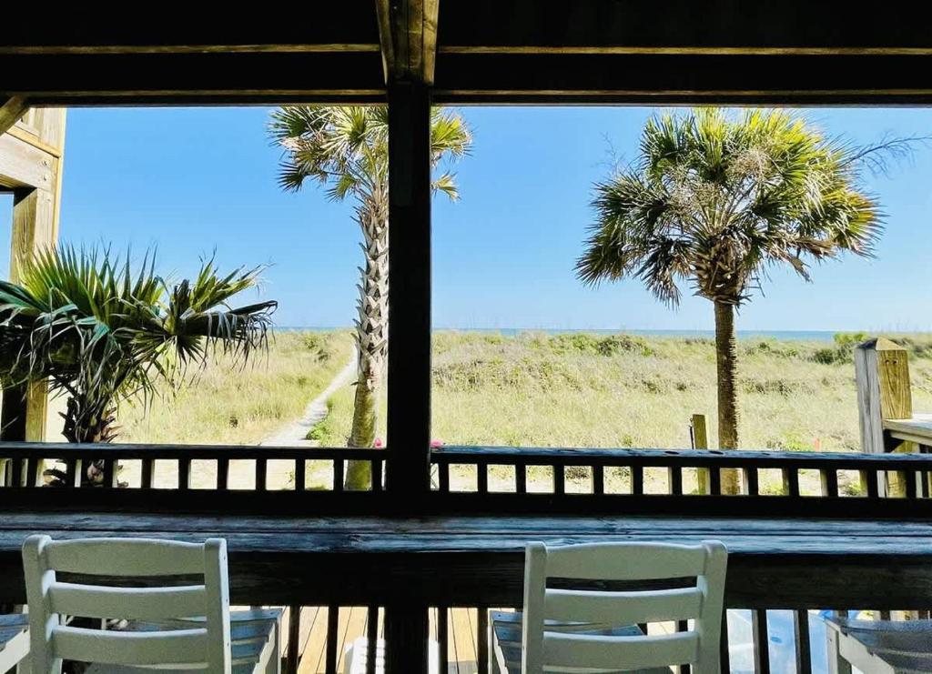 zwei weiße Stühle auf einer Veranda mit Palmen in der Unterkunft OCEANFRONT HOUSE ON THE SAND 2 Kings 4br 4ba 1st Floor of Triplex SLEEP 12 PGP1 in Myrtle Beach