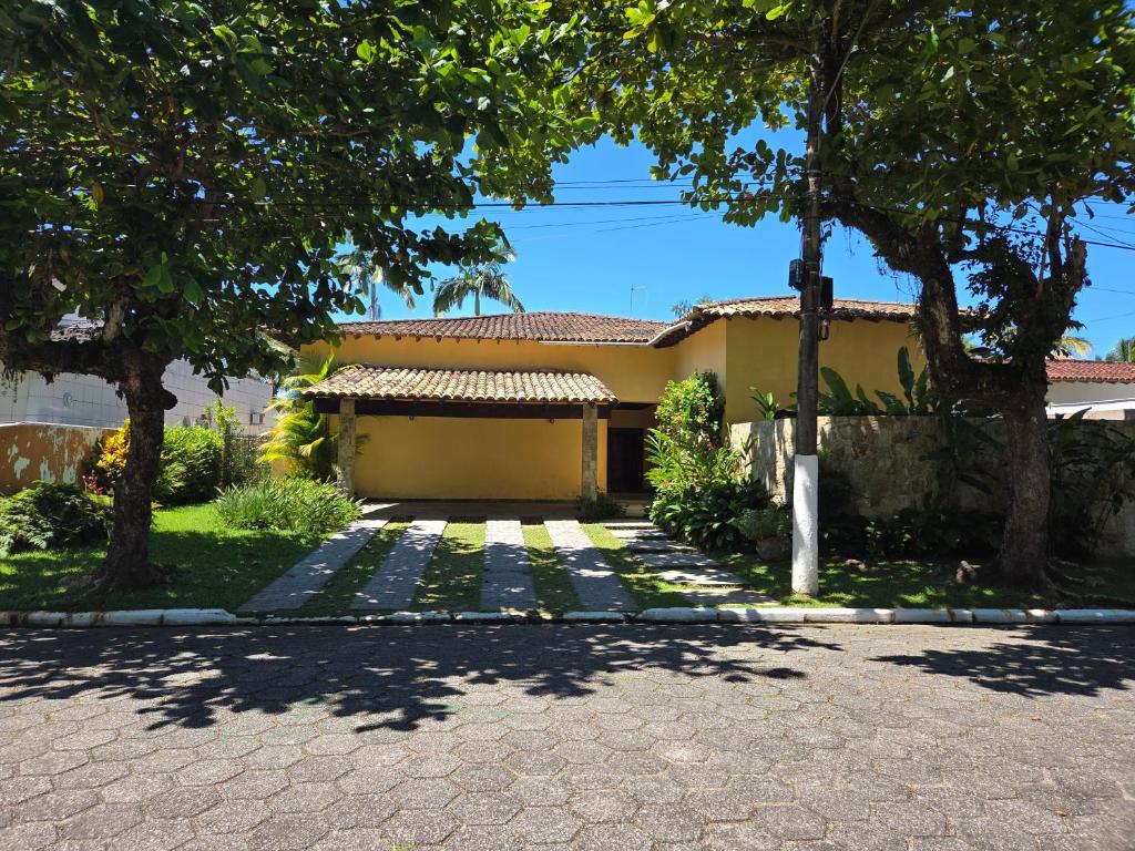 a yellow house with trees and a driveway at Casa Praia Jardim Acapulco in Guarujá