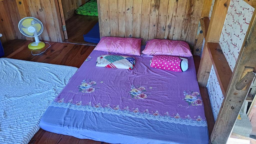 un letto in una stanza di legno con lenzuola e cuscini viola di Bhev's Buscalan Homestay a Tinglayan