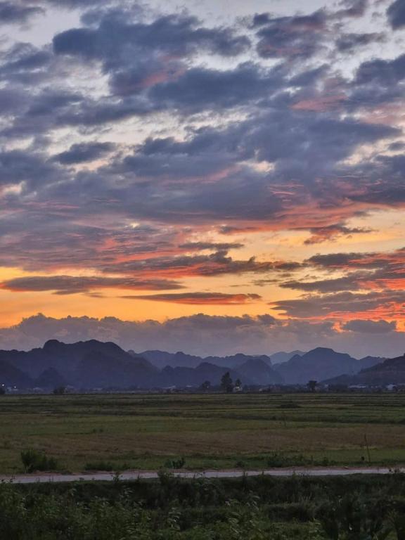 una puesta de sol sobre un campo con montañas en el fondo en Palafita Bungalow, en Bố Trạch