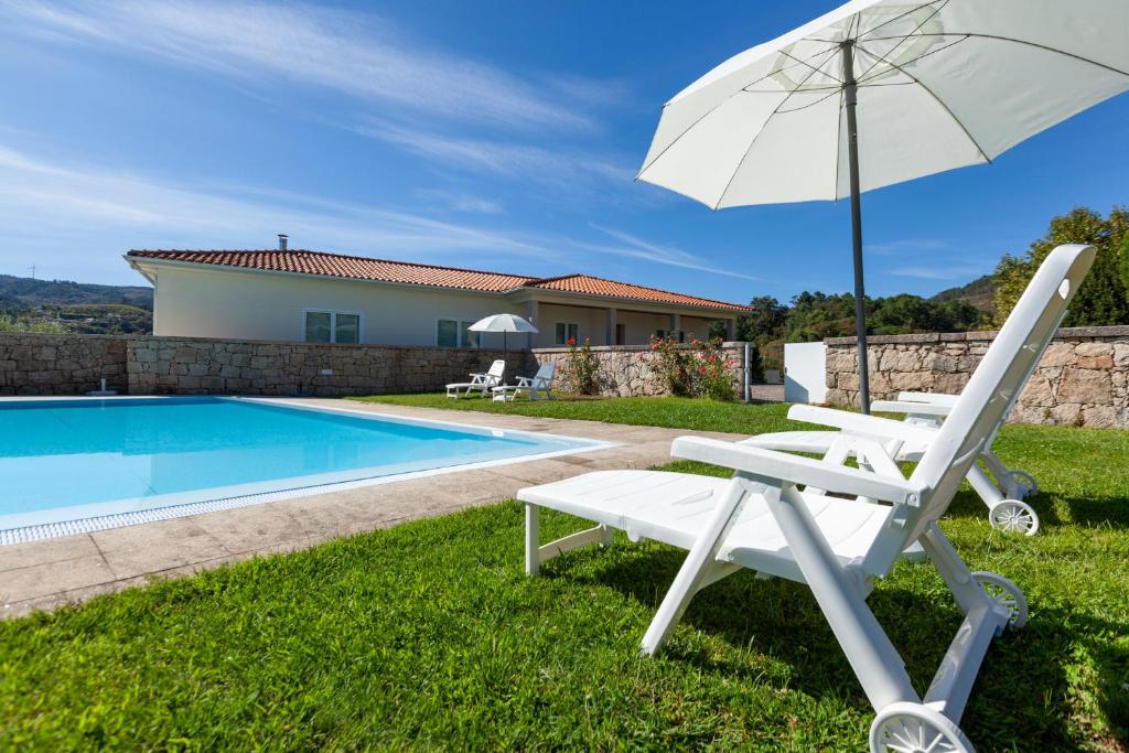 een witte ligstoel met parasol naast een zwembad bij Casa Panorâmica Aurora in Celorico de Basto