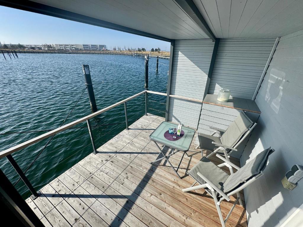 a boat deck with a table and chairs on the water at Hausboot Lilla Lina in Fehmarn