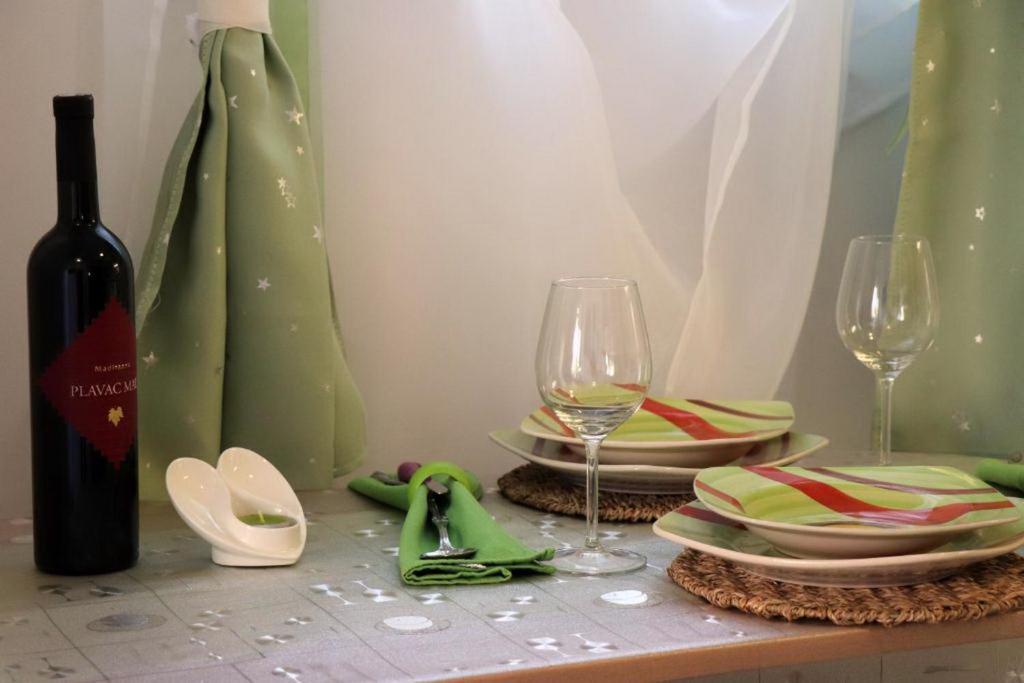 a table with two glasses and plates and a bottle of wine at Apartmani clementina sunrise in Orebić