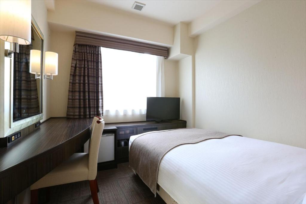 a hotel room with a bed and a desk with a television at Hotel Hokke Club Niigata Nagaoka in Nagaoka