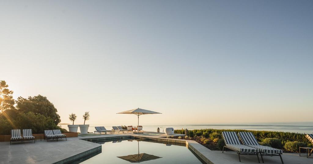a swimming pool with chairs and an umbrella at Casa Pôr do Sal in Luz