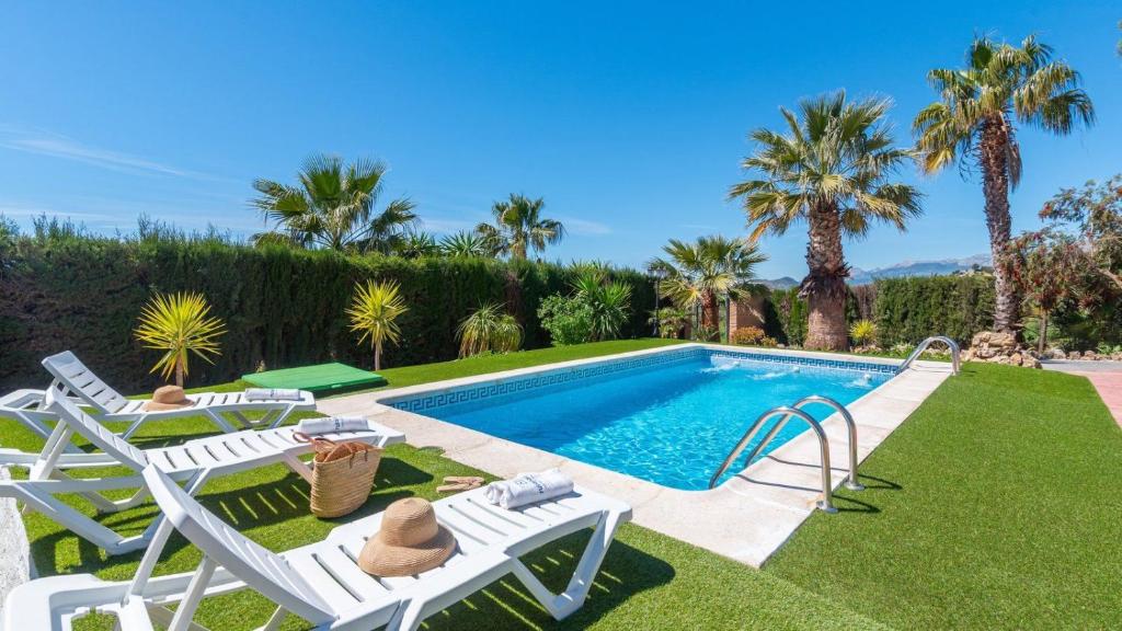 a swimming pool with chairs and a lawn with palm trees at Cortijo El Púlpito Periana by Ruralidays in Periana