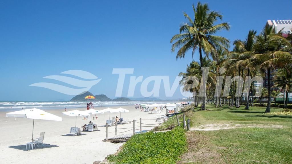 a beach with palm trees and people sitting under umbrellas at Travel Inn Flats Riviera in Riviera de São Lourenço
