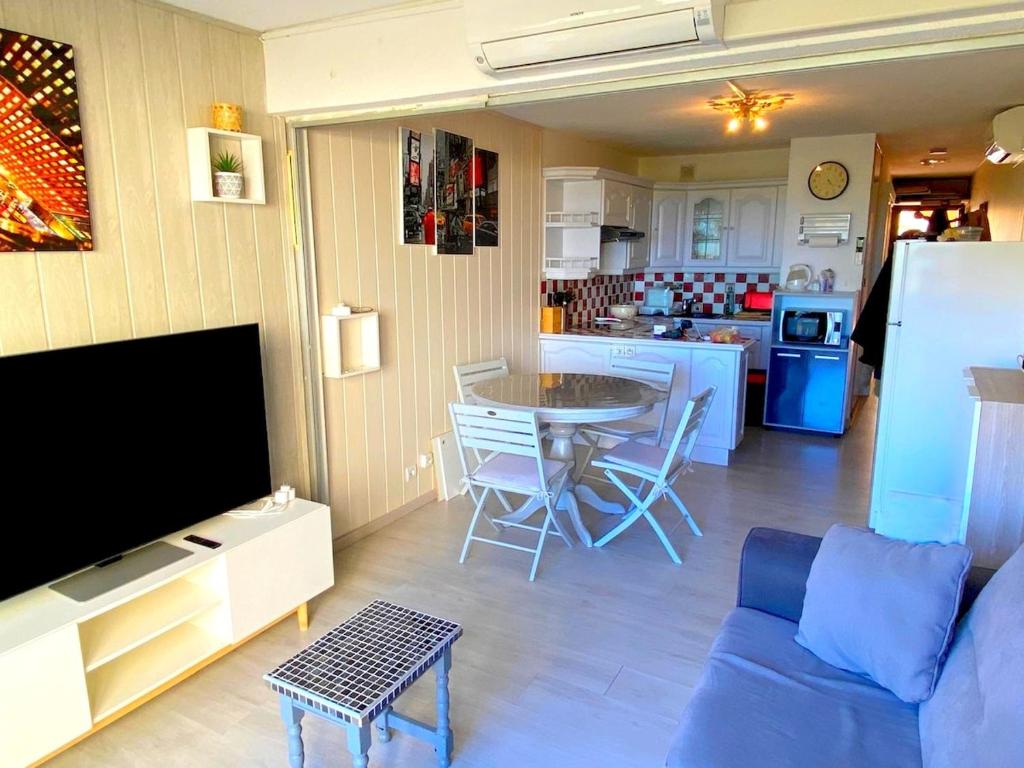 un salon avec un canapé bleu et une cuisine dans l'établissement T2 Leucate climatisé - Vue mer, piscine et plage, à Leucate-Plage