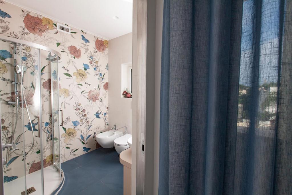 a bathroom with a shower and a toilet with floral wallpaper at Dimora Nesea in Cozze