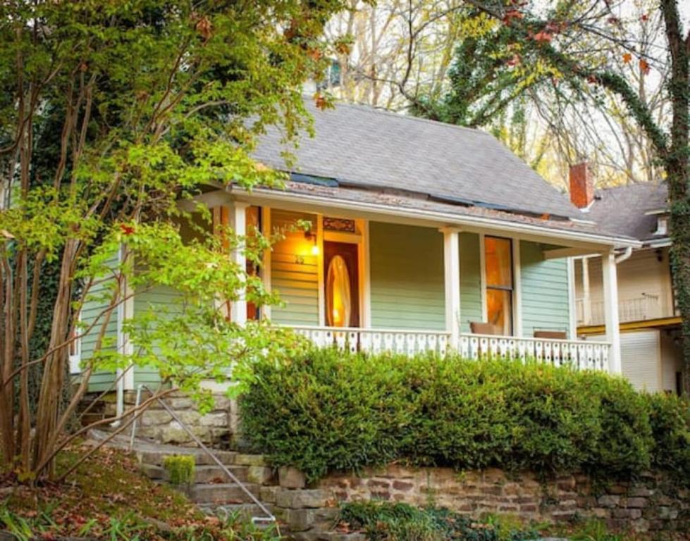 a white house with a porch and a stone wall at Cricket Cottage in Eureka Springs