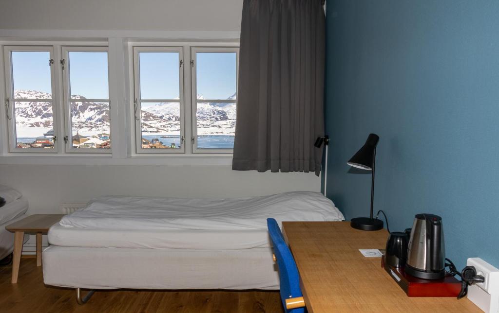 a bedroom with a bed and a table and windows at Hotel Angmagssalik in Tasiilaq