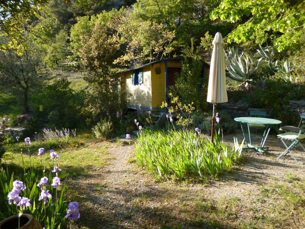 un jardín con mesa, sombrilla y flores en Roulotte, en Aubres