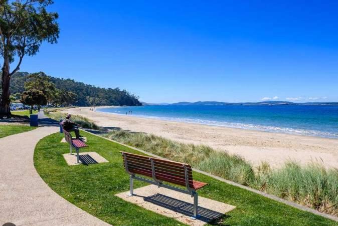 two benches sitting on the grass near the beach at Ocean Views 20kms from CBD Sleeps 10 in Kingston Beach