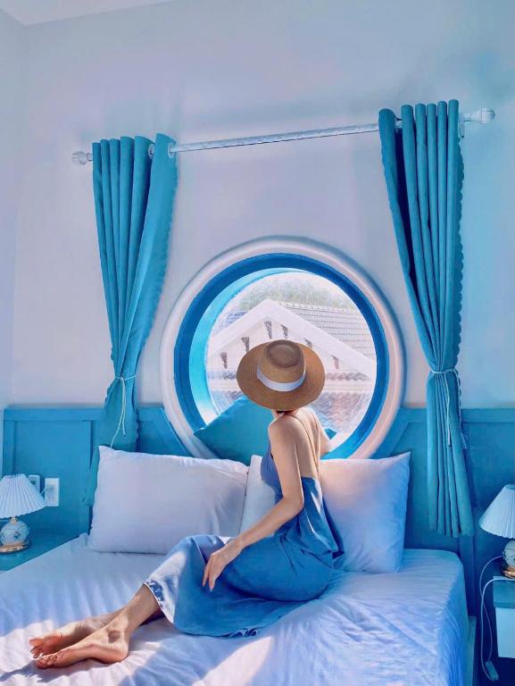 a woman in a straw hat sitting on a bed at Robinson Homestay - Cù Lao Mái Nhà in Tuy An