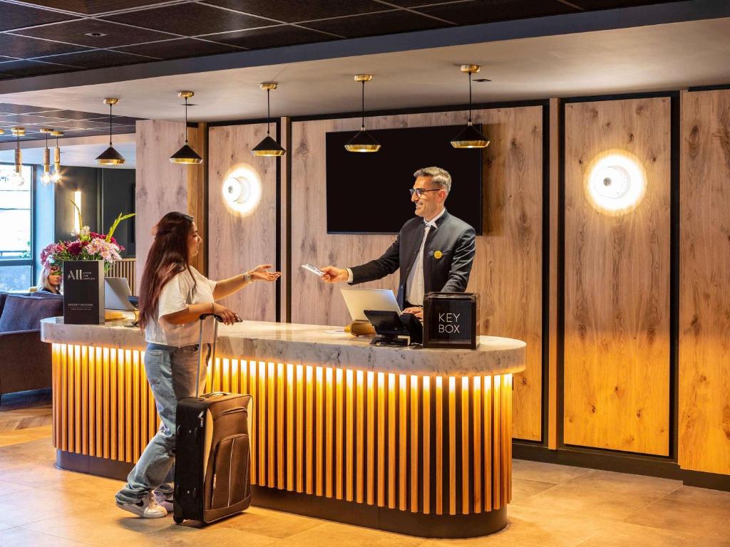 a man and a woman standing at a counter at Novotel Birmingham Airport Terminal Building - NEC in Bickenhill