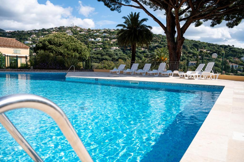 - une piscine avec des chaises blanches et un arbre dans l'établissement Alora - Superbe Studio Vue Mer Climatisé avec Piscine, à Cavalaire-sur-Mer