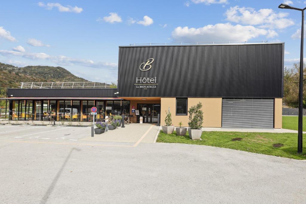 a hotel with a black roof and a parking lot at Hôtel Restaurant AKENA Molinges - La Brocatelle in Saint-Claude