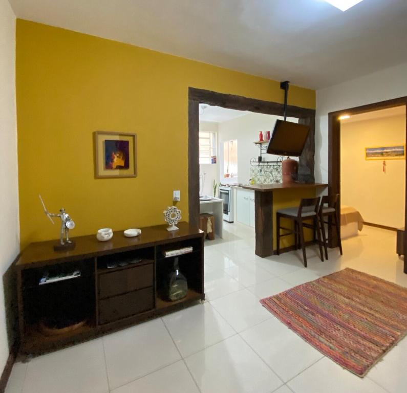a living room with a yellow wall and a kitchen at Apartamento no Centro Histórico in São João del Rei