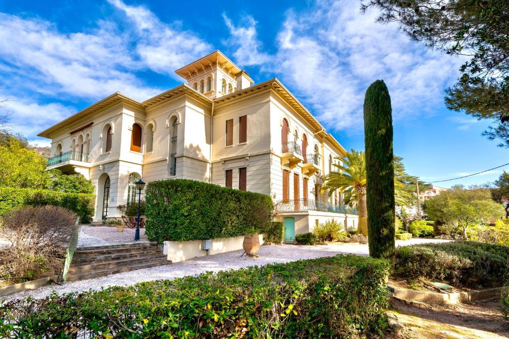 une grande maison blanche avec des arbres devant dans l'établissement 3 pièces élégant - Clim Terrasse Parking - Plage, à Saint-Raphaël