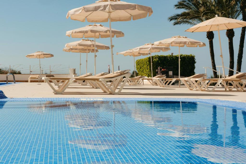 a swimming pool with chairs and umbrellas at Minura Sur Menorca in Punta Prima