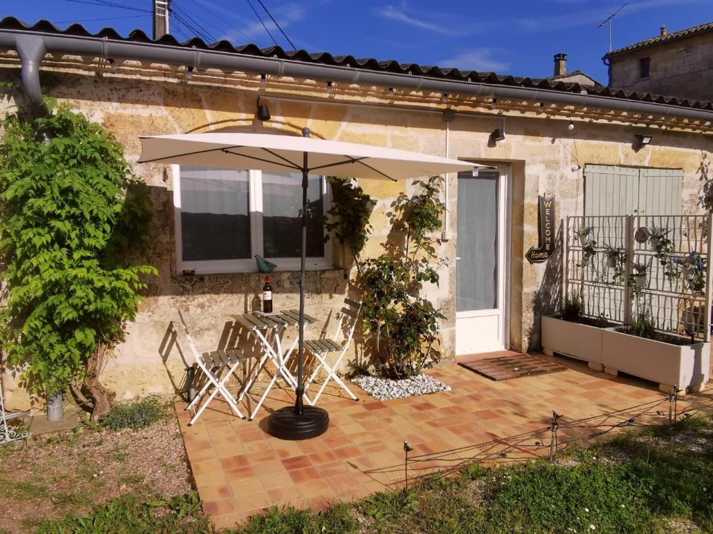 - une terrasse avec un parasol et des chaises en face d'une maison dans l'établissement Proche Saint-Émilion, confortable gîte rénové avec terrasse - 2 personnes, à Sainte-Terre