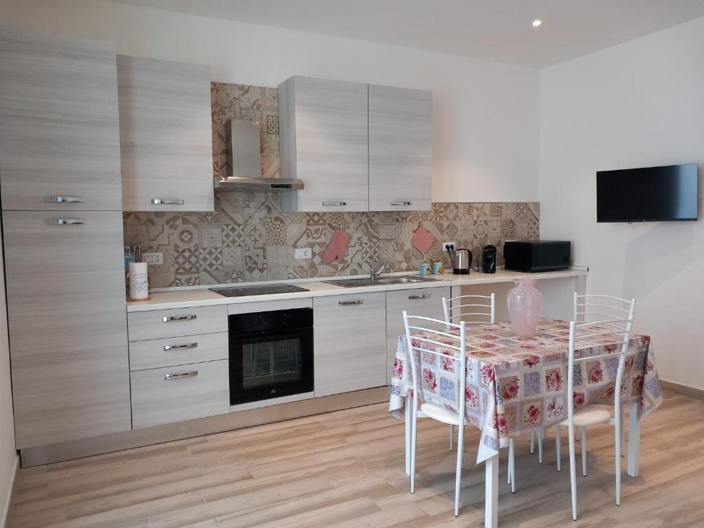 una cocina con mesa con sillas y una cocina con armarios blancos. en Il Sogno di Francesca, en Alghero