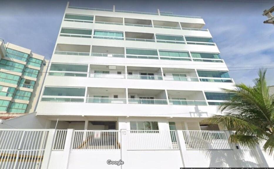 Un edificio alto y blanco con una palmera delante. en Apartamento na Orla da Praia Grande para até 6 pessoas - Arraial do Cabo, en Arraial do Cabo