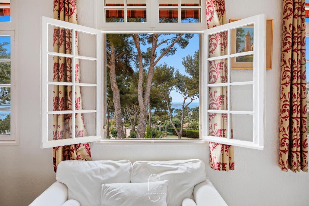 - une fenêtre avec des rideaux et un canapé en face dans l'établissement T3 L'escapade Mont des oiseaux Piscine Clim Parking By HC, à Hyères