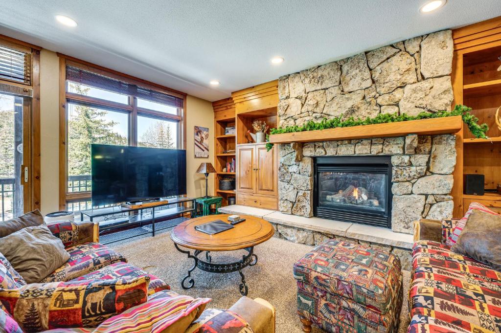 a living room with a stone fireplace and a tv at Walk to Gondola Condo with Deck in Winter Park! in Winter Park