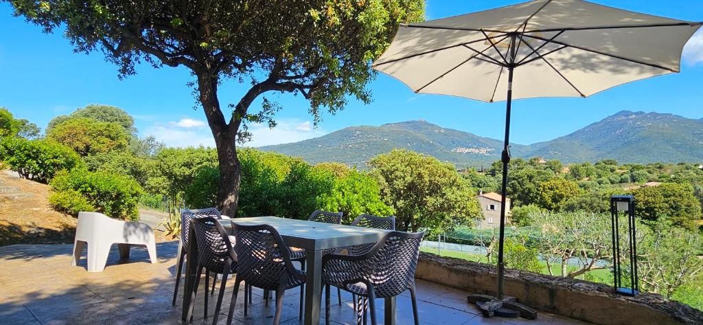 a table and chairs with an umbrella and mountains at T3 Dolce & Vita D5 avec Piscine et vue Montagnes in Propriano