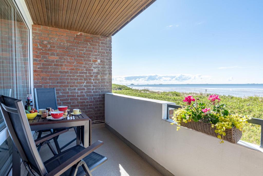 a balcony with a table and flowers and a view of the ocean at Dünennest in Südstrand