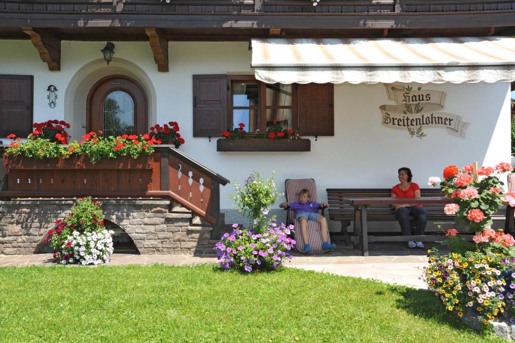 une femme et un enfant assis sur un banc devant une maison dans l'établissement Pension Breitenlohner, à Reit im Winkl