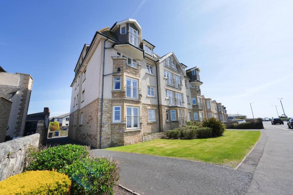 a large brick building with a grass yard in front of it at Caledonia by the Sea in Saltcoats