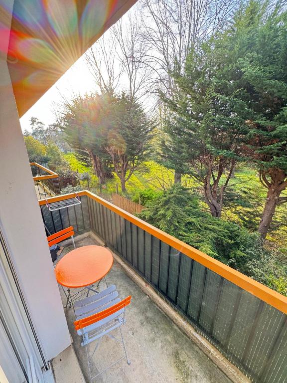 un balcon avec une table et des chaises orange et des arbres dans l'établissement Le Champenois, plage et calme, à Merville-Franceville-Plage