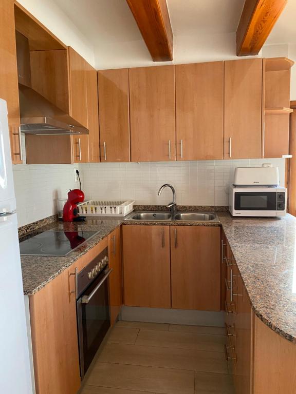 a kitchen with wooden cabinets and a sink and a microwave at Apartamentos LLorca in Platja de l’Almadrava